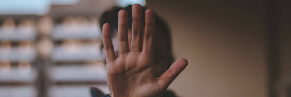Image of a man with his hand forward, hiding his face